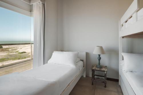 a white bedroom with a bed and a window at MarAdentro Apart Hotel & Suites in Punta Del Diablo