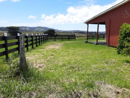 a fence next to a red barn in a field at Cabañas MAR BRAVA in Ancud