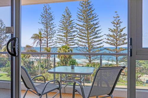 a table and chairs on a balcony with a view of trees at Northwind Beachfront Apartments in Mooloolaba