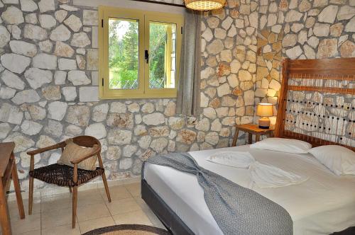 a bedroom with a stone wall with a bed and a chair at Stone Villa Kefaloniaprivatevillas in Trapezaki
