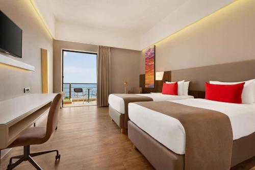 a hotel room with two beds and a desk and a balcony at Ramada Plaza by Wyndham Thraki in Alexandroupoli