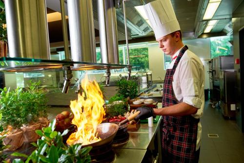 a chef preparing food in a kitchen with a fire at Sound Garden Hotel Airport in Warsaw