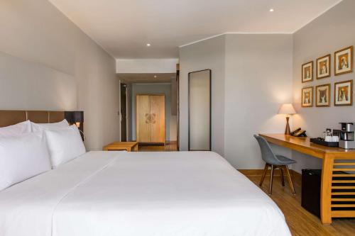a hotel room with a large white bed and a desk at Radisson Hotel Tamboho Waterfront Antananarivo in Antananarivo
