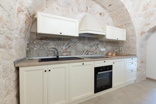 a kitchen with white cabinets and a stone wall at Trulli in Vigna in Selva di Fasano
