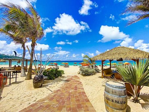 uma praia com cadeiras e palmeiras e o oceano em Maracuja 4, Orient Bay village, walkable beach at 100m em Orient Bay