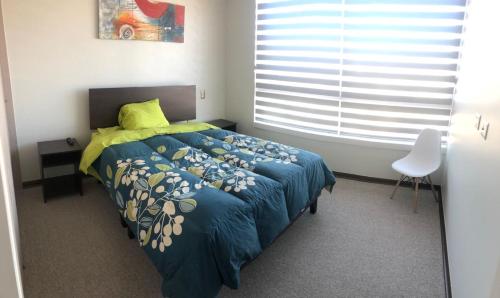 1 dormitorio con 1 cama con edredón azul y ventana en Departamento Familiar con vista al Mar, en Coquimbo