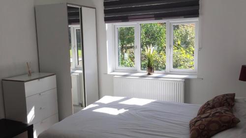 a bedroom with a white bed and two windows at Quiet Studio by Lloyd Park in South Norwood