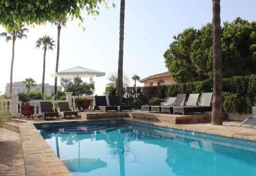 a swimming pool with chairs and an umbrella and palm trees at Rustic spanish villa Saltwater Pool in Benalmádena
