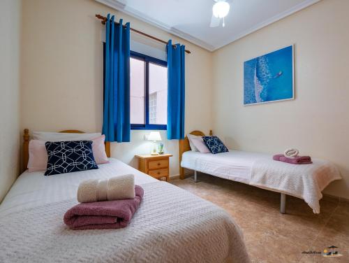 two beds in a room with blue curtains at Apartment Eva Cabo Roig in Cabo Roig