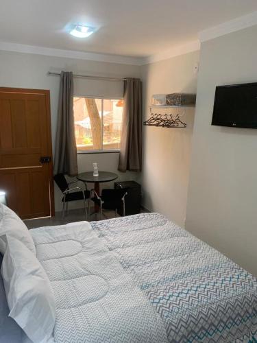a bedroom with a bed and a table and a window at Ipê Suítes in Domingos Martins