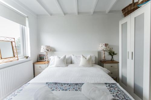 a white bedroom with a large bed and a window at Fairlight - Charming coastal home on the beach in Chichester