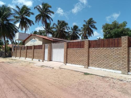 a brick fence next to a dirt road with palm trees at Pousada Villa Manduca in Amontada