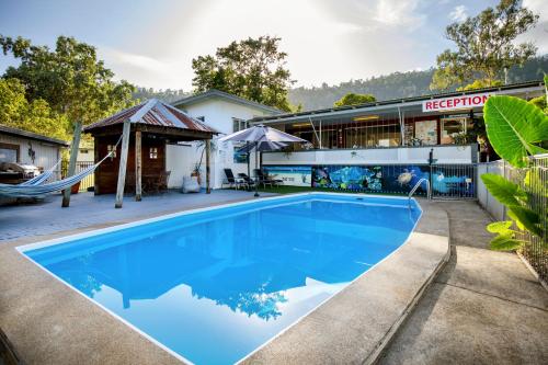 a swimming pool in front of a house with a hammock at Bush Village Holiday Cabins in Airlie Beach