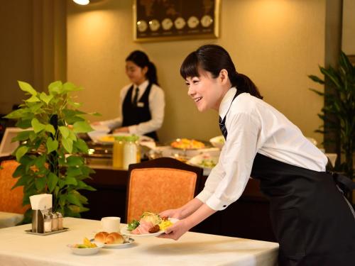 a woman standing over a table with a plate of food at Pulses Inn Kyoto in Kyoto