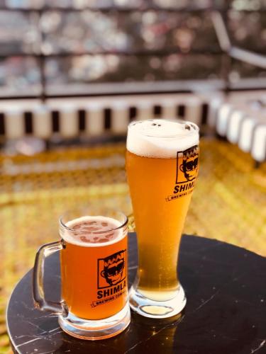 two glasses of beer sitting on top of a table at Hotel Willow Banks Shimla in Shimla