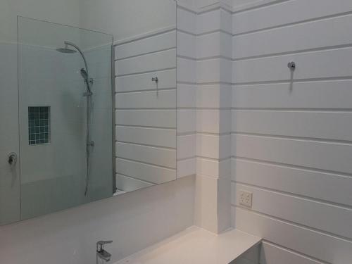 ein weißes Bad mit einer Dusche und einem Spiegel in der Unterkunft Little Cove Townhouse 5 Pandanus Street 14 in Noosa Heads