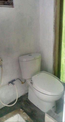 a bathroom with a white toilet and a hose at De Ikut Bojo Homestay in Magelang