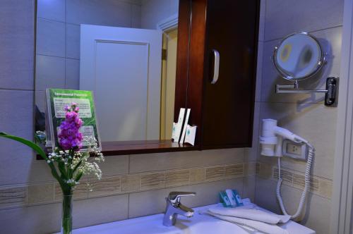 a bathroom sink with a mirror and a vase of flowers at Comfort Hotel Suites in Amman