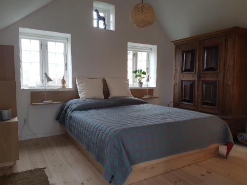 a bedroom with a bed with a blue comforter and two windows at Fiskerhuset in Agger