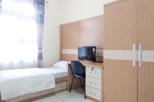 a bedroom with a bed and a desk with a television at Griya De Riz Syariah Mitra RedDoorz in Jambi