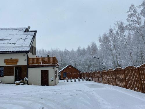 a snow covered yard with a fence and a house at Agroturystyka Blicharzówka Noclegi in Bukówka