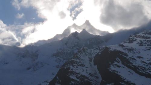 a mountain covered in snow and clouds in the sky at Amor Lodge in Saas-Fee