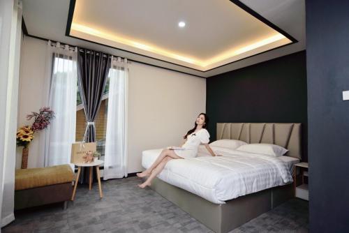 una mujer sentada en una cama en una habitación de hotel en เขาค้อ บาร์ล้านวิว Barlanview en Khao Kho