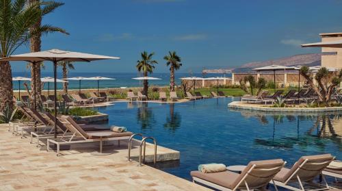 a swimming pool with chairs and umbrellas and the ocean at Fairmont Taghazout Bay in Taghazout