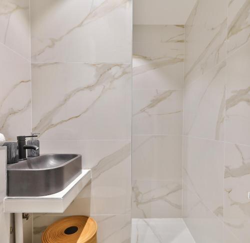 La salle de bains est pourvue d'un lavabo et de murs en marbre blanc. dans l'établissement 97 - Urban Colonnes de Buren, à Paris