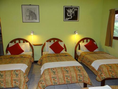 a room with three beds with red and white pillows at Hotel Jaguar Inn Tikal in Tikal