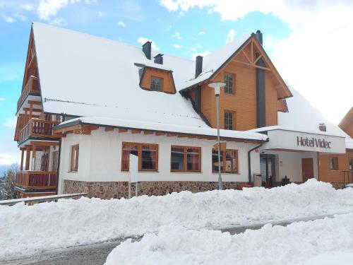 a building covered in snow next to a pile of snow at Pohorje Village Wellbeing Resort - Forest Hotel Videc in Pohorje