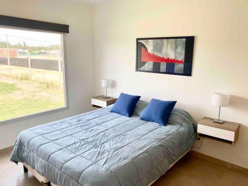 a bedroom with a bed with blue pillows and a window at Casa con pileta y parrilla en barrio privado, 2 dormitorios in General Roca