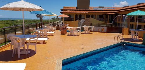 a balcony with a swimming pool and tables and umbrellas at Pousada Ilha Bella in Guriri