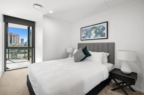 a white bedroom with a large bed and a window at Koko Broadbeach in Gold Coast