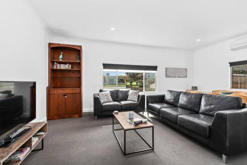a living room with a black leather couch and a tv at Kokomo - Silver Sands - C21 SouthCoast Holidays in Aldinga Beach