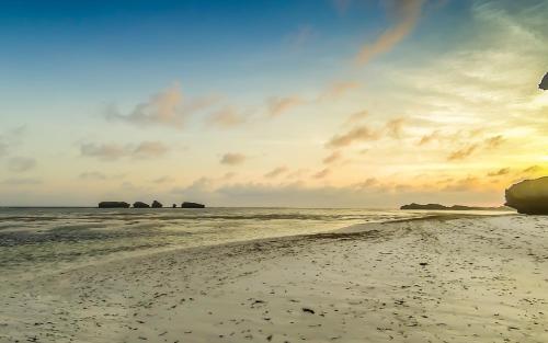 a beach with rocks in the water and a sunset at The Charming Lonno Lodge Watamu in Watamu