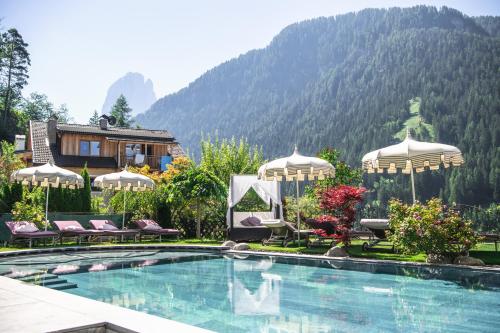 a swimming pool with chairs and umbrellas in front of a mountain at Alpin Garden Luxury Maison & SPA - Adults Only in Ortisei