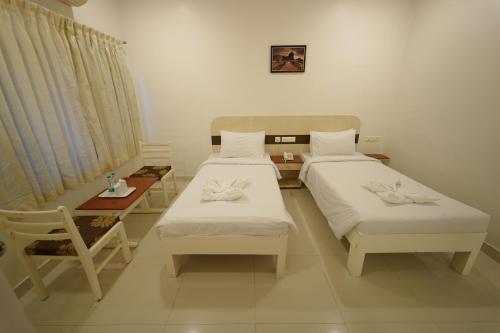 two beds in a room with a table and a bed sidx sidx sidx at Hotel Palmyra Grand Inn in Tirunelveli