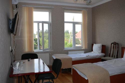 a room with two beds and a table and two windows at Beylagan Naftalan Hotel in Beylǝqan
