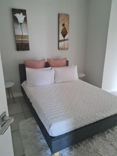 a bedroom with a bed with white sheets and pink pillows at Luxury 264 The Blyde in Pretoria