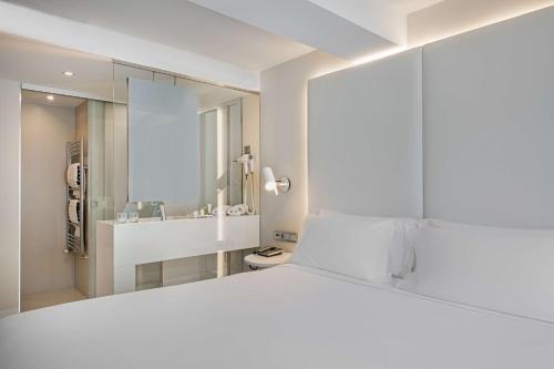 a white bedroom with a large white bed and a mirror at NH Paseo de la Habana in Madrid