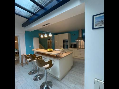 een keuken met blauwe muren en een eiland met barkrukken bij Balaena - maison avec jardin proche plage in Luc-sur-Mer