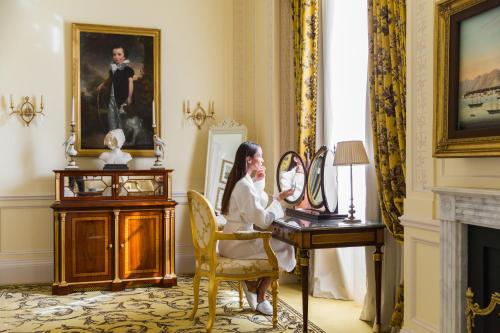 a woman sitting at a desk in a room with a painting at The Lanesborough, Oetker Hotels in London