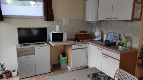 a small kitchen with white cabinets and a television at Fenyves-lak in Szalkszentmárton