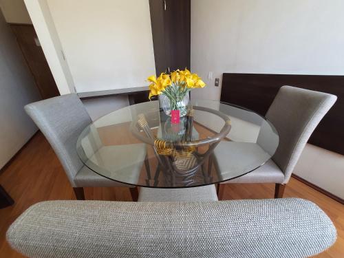 a glass table with a vase of yellow flowers on it at Hotel Capelli Express in Talca