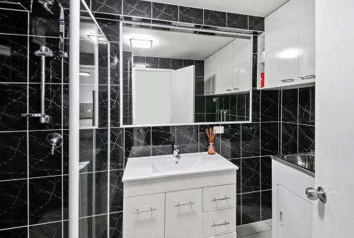 Baño de azulejos negros con lavabo y espejo en Paradis Pacifique, en Maroochydore