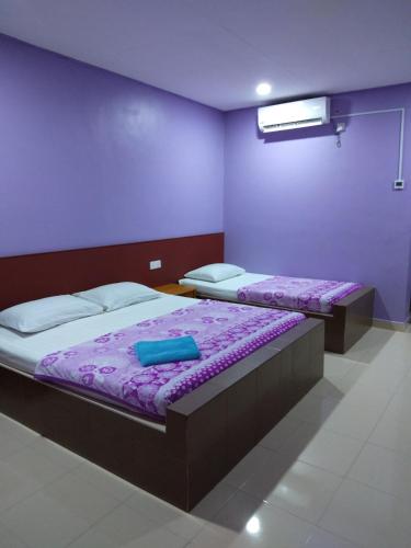 two beds in a room with purple sheets at Inapan Aishah in Pantai Cenang