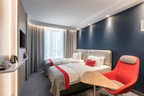 a hotel room with two beds and a red chair at Holiday Inn Express - Kaiserslautern by IHG in Kaiserslautern