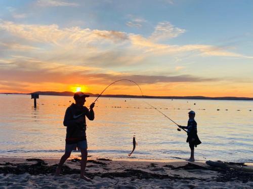 two people fishing on the beach at sunset at Nuts About the Bay in Nelson Bay