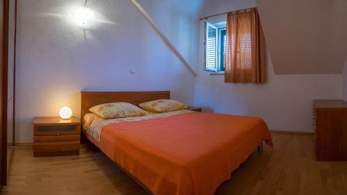 ein Schlafzimmer mit einem Bett mit einer orangefarbenen Decke und einem Fenster in der Unterkunft Apartments Pipo in Pučišća